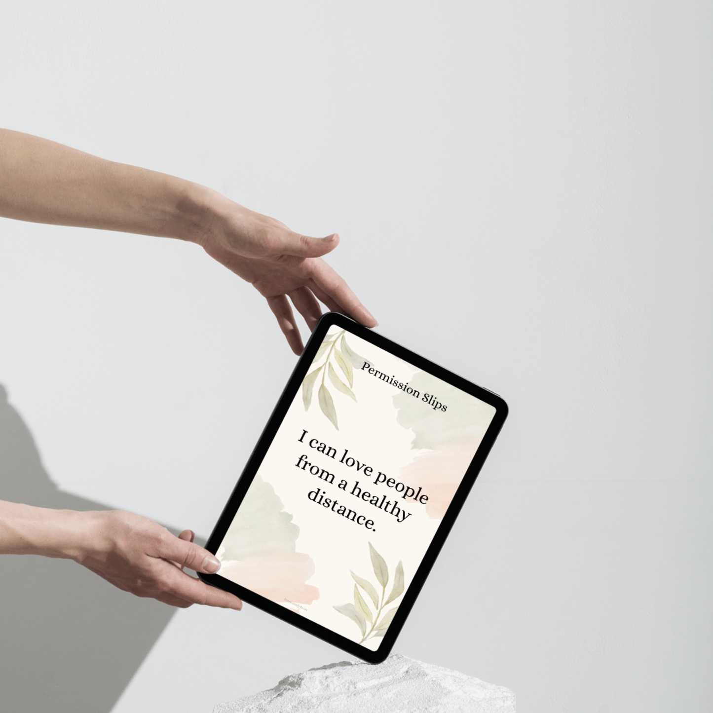 A hand holding a tablet showing an affirmation card that reads ‘I can love people from a healthy distance.