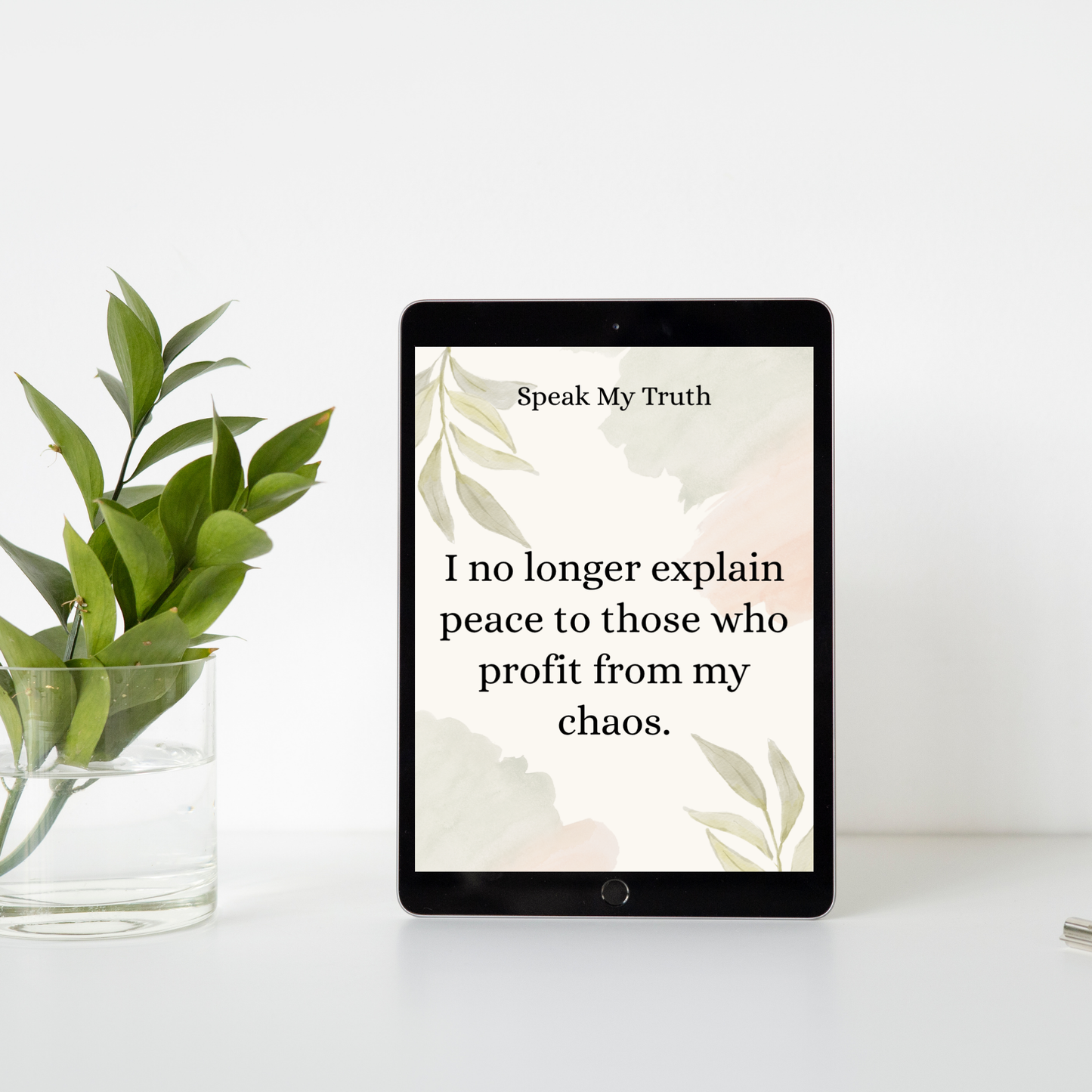 Digital affirmation card displayed on a tablet beside a clear vase with green leaves against a white wall.
